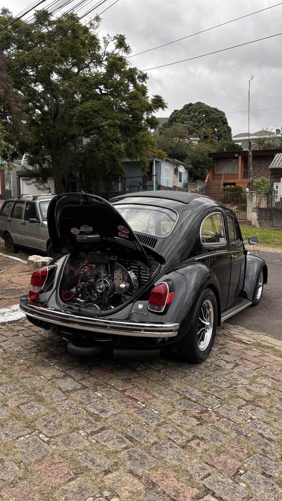 Fusca preto com o capô traseiro aberto mostrando o motor, na rua de paralelepípedos